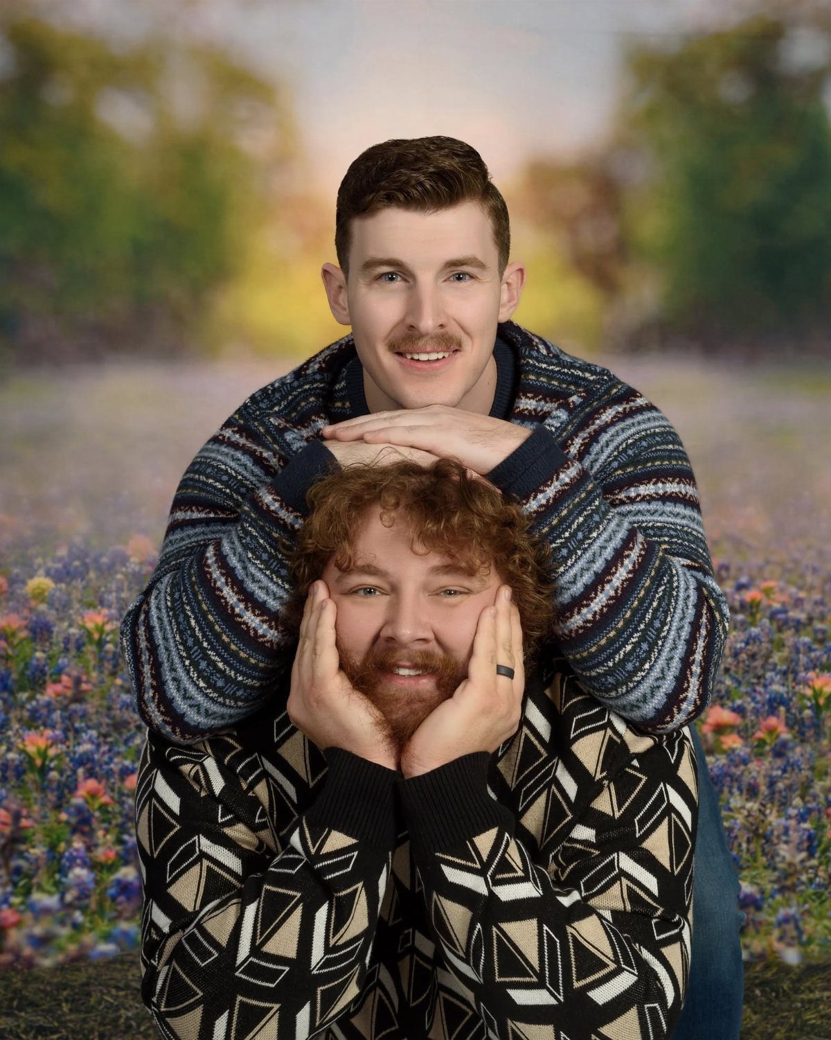 Two men in patterned sweaters posing awkwardly against a blurred nature backdrop.