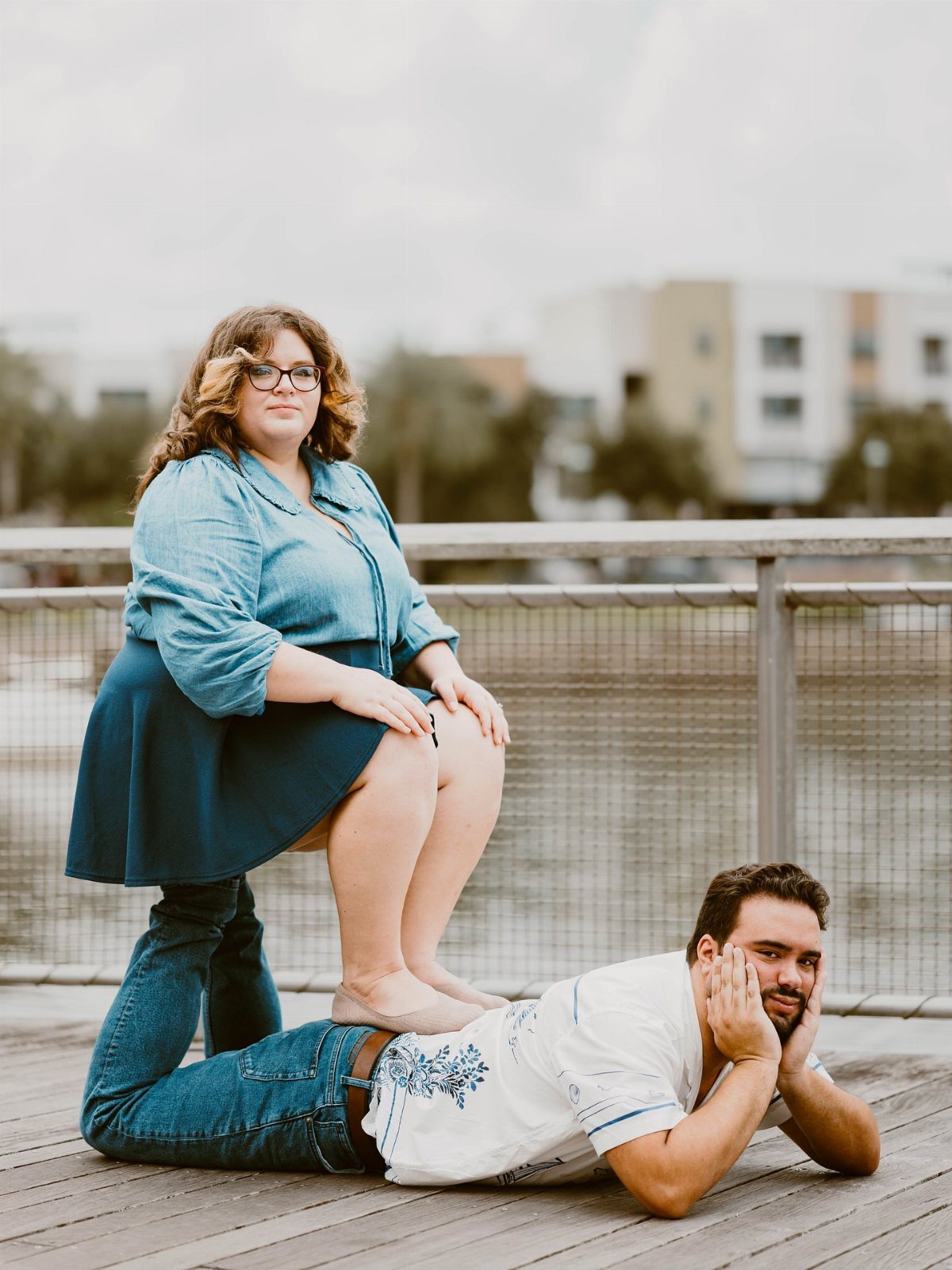 Woman sitting on a man's back while he lies on a wooden deck.