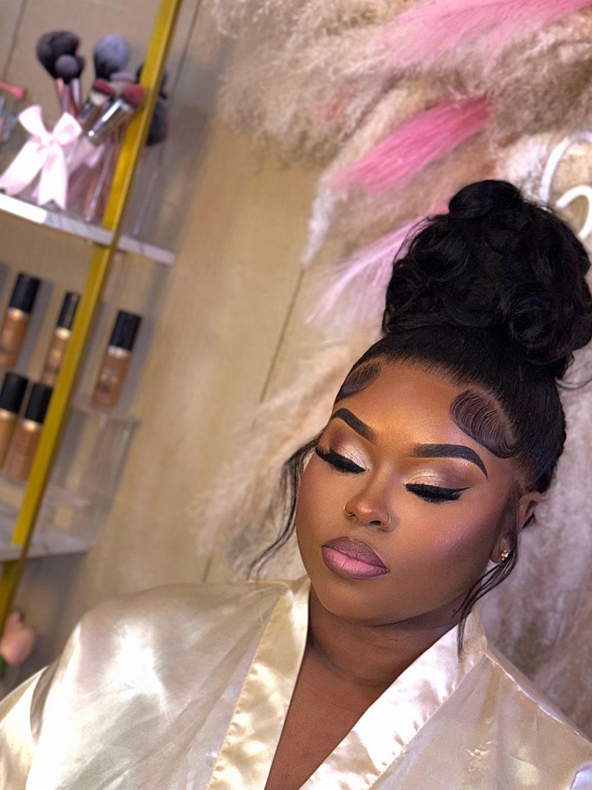 Woman with a high curly bun and bridal makeup wearing a white satin robe.