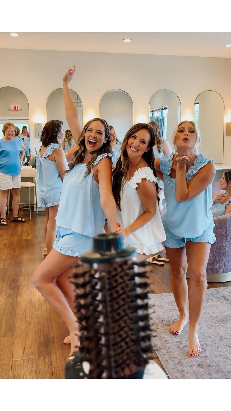 Three women in bridal party pajamas laughing in a room with arched mirrors.