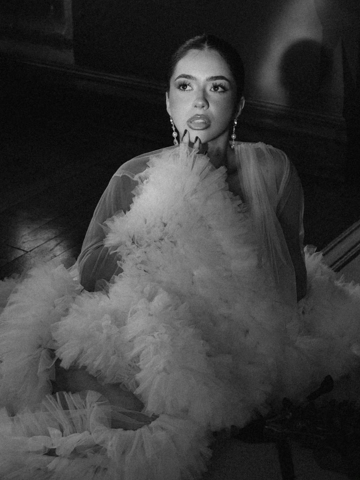 Bride in a ruffled white wedding gown posing for a black and white portrait.