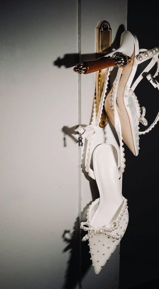 White pearl-embellished bridal heels hanging from a gold door handle.