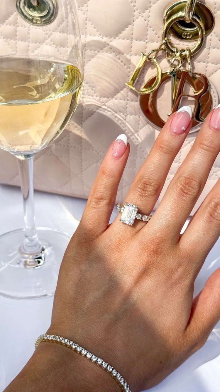 Woman's hand with diamond engagement ring, tennis bracelet, white wine, and Dior bag.