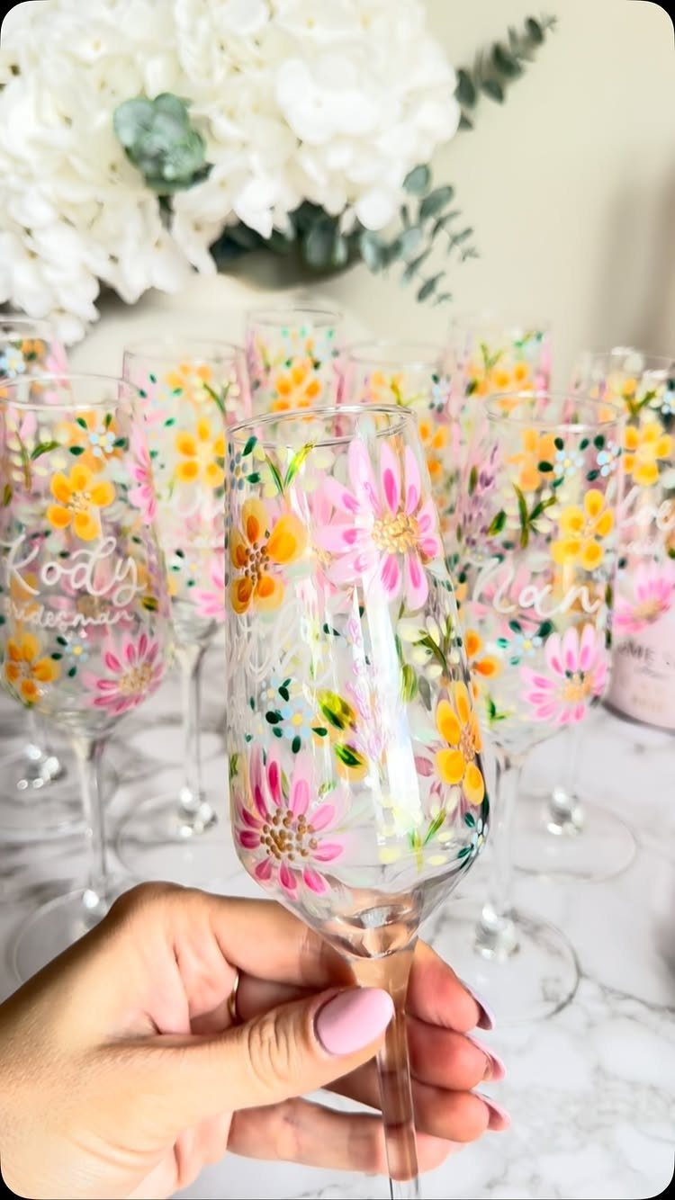 Floral painted champagne flutes on a marble surface with white flowers in background