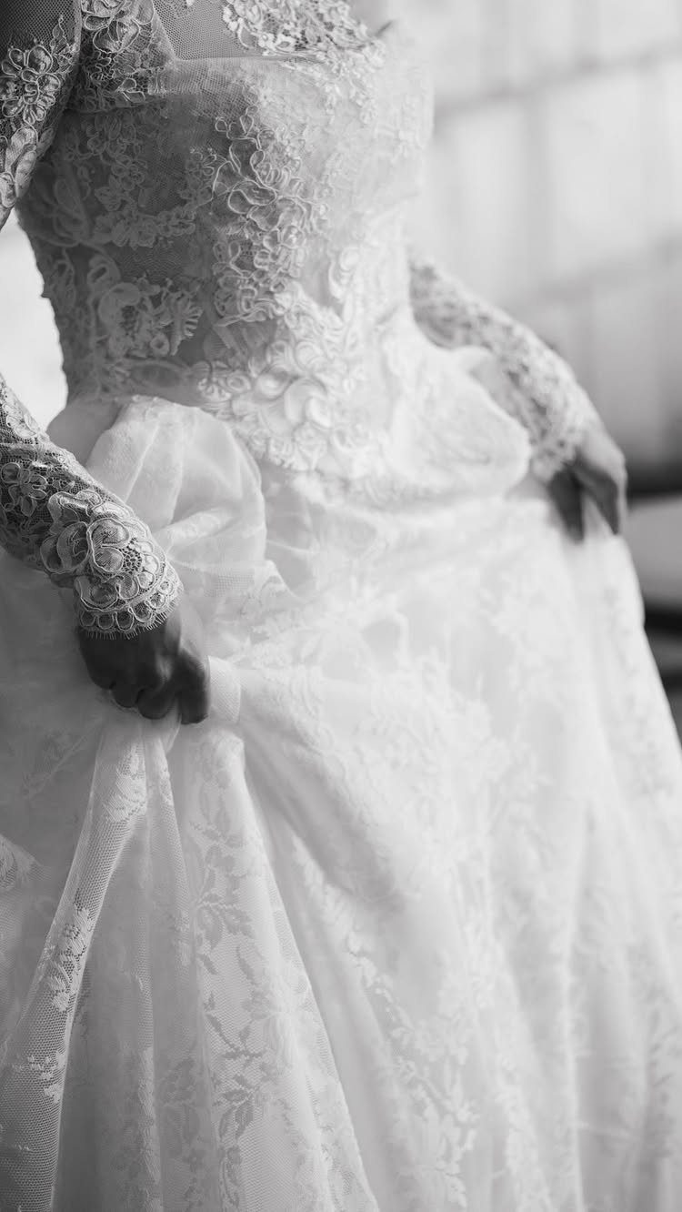 Bride in a long-sleeved lace wedding dress holding the fabric of her skirt.