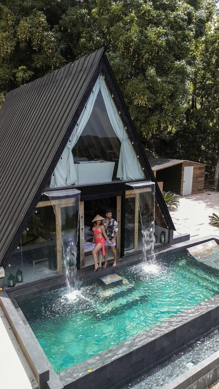 Couple standing by a turquoise plunge pool in front of a modern A-frame cabin.