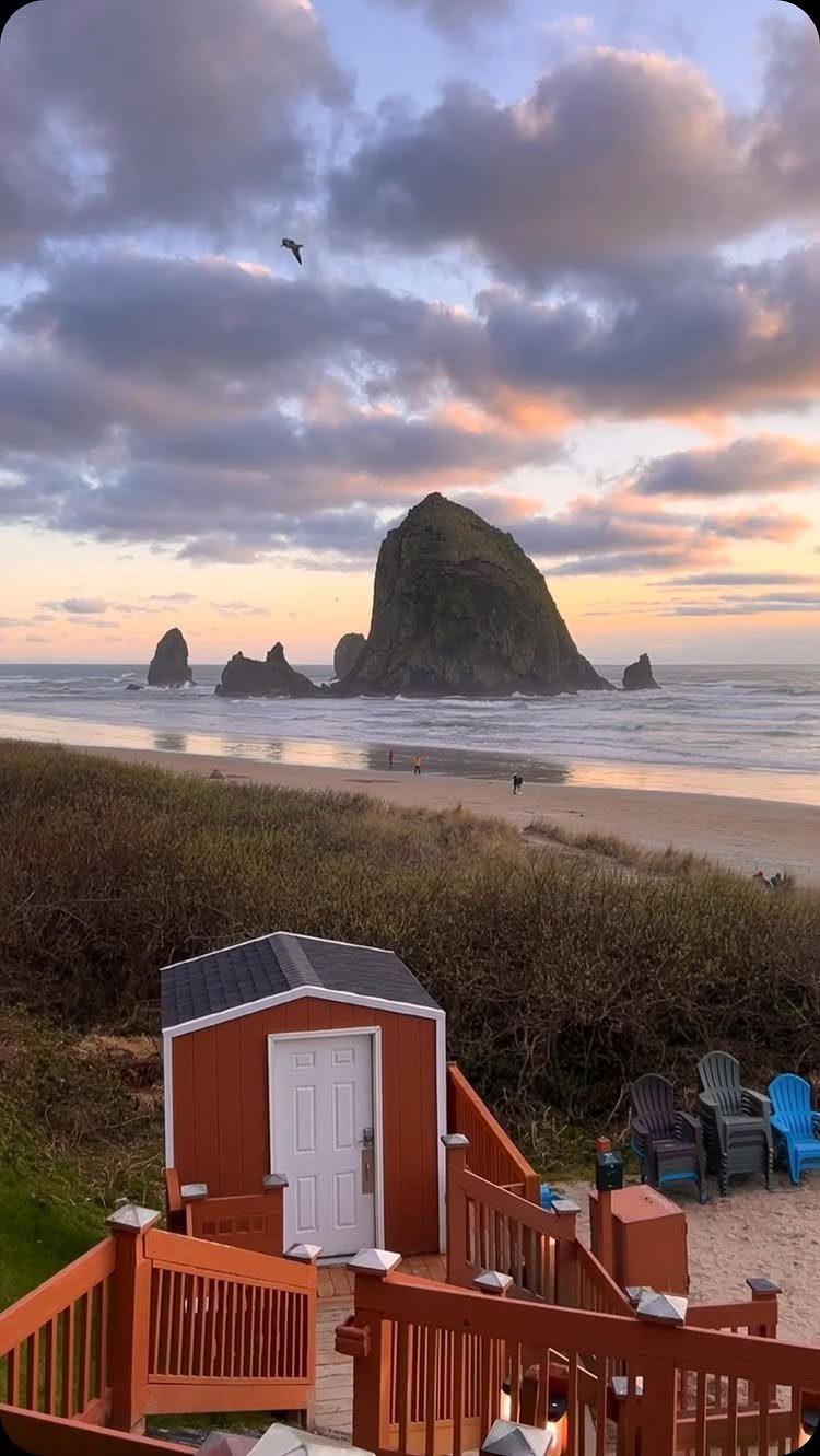 Large sea stack rock on a sandy beach viewed from a wooden deck.