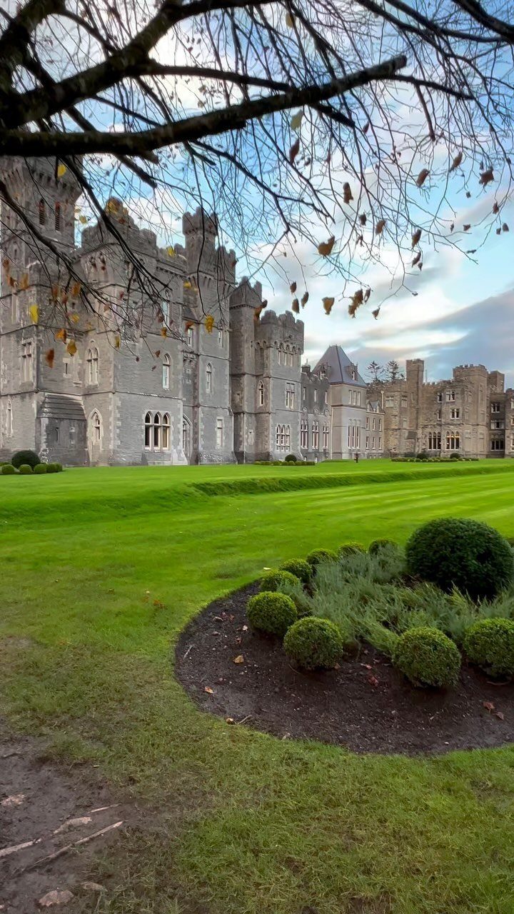 Large grey stone castle with towers overlooking a lush green manicured lawn