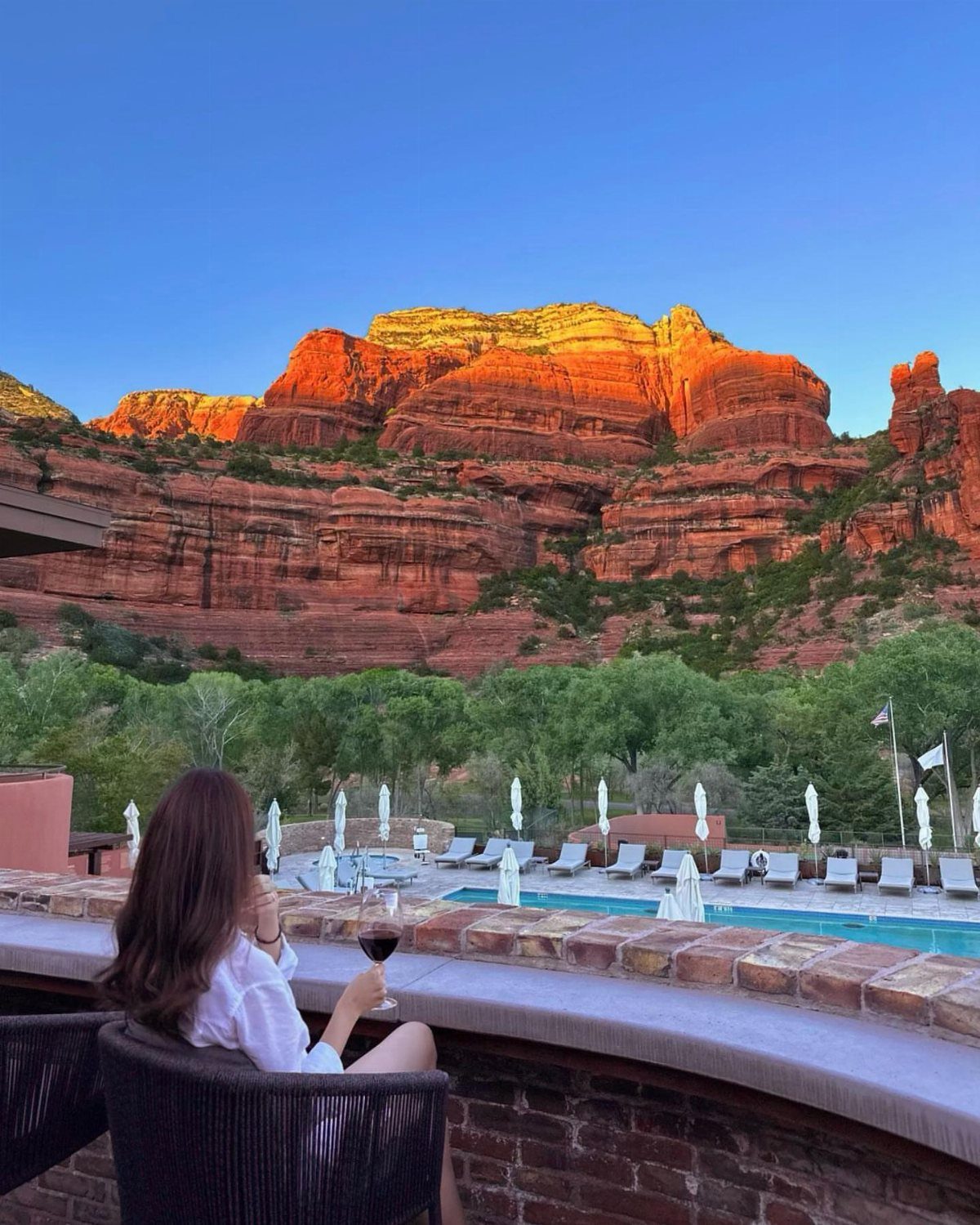 Woman drinking wine on a terrace overlooking a pool and red rock formations.