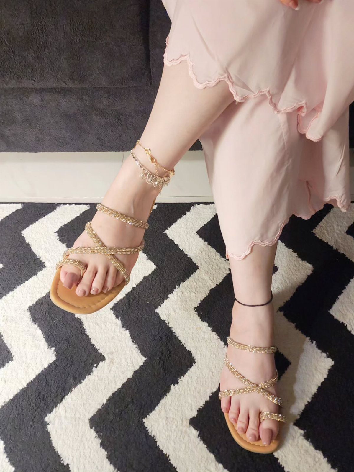 Gold braided strap sandals and a gold chain anklet on a person's feet