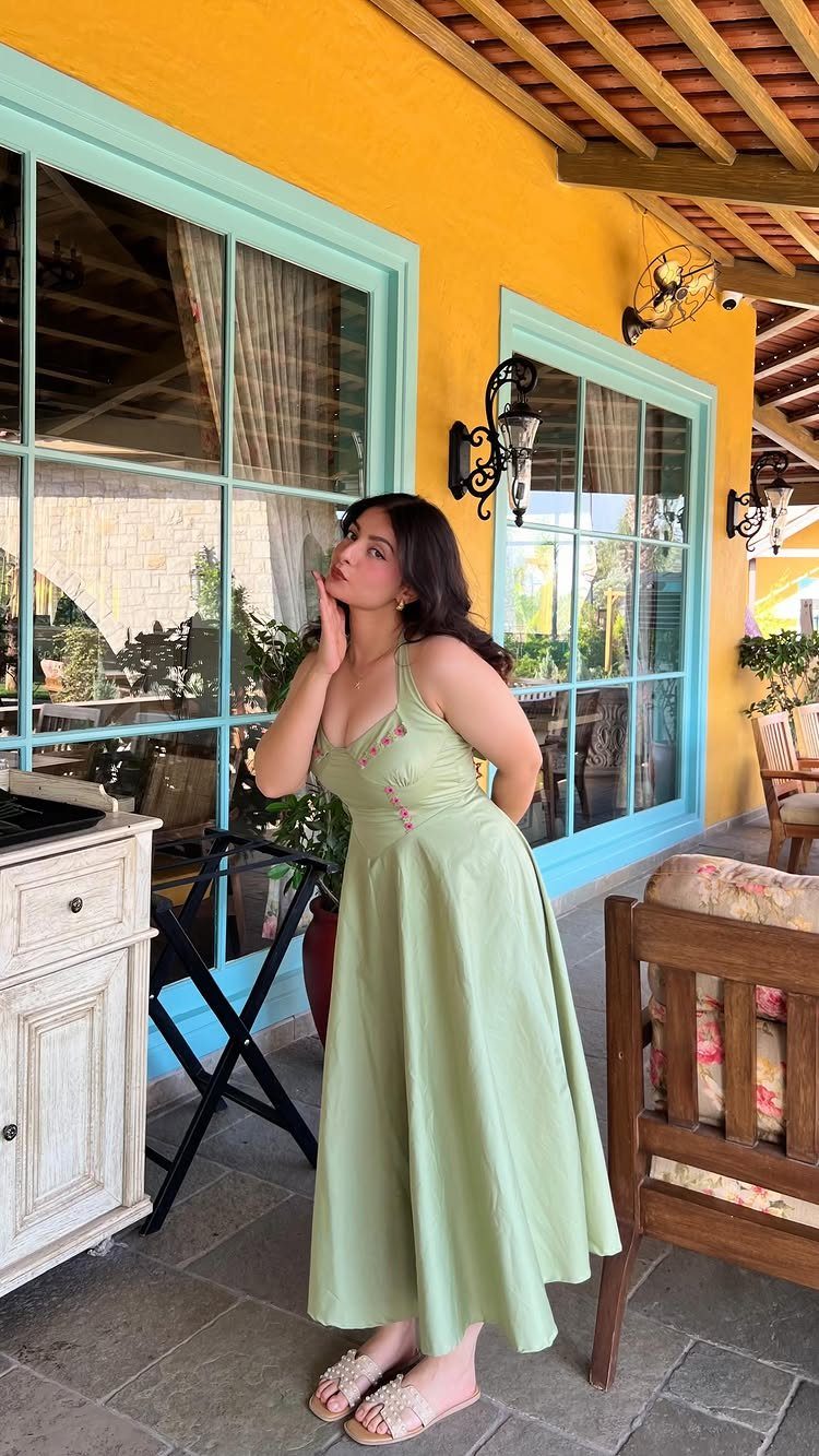 Woman in a sage green halter-neck sundress posing by a yellow wall