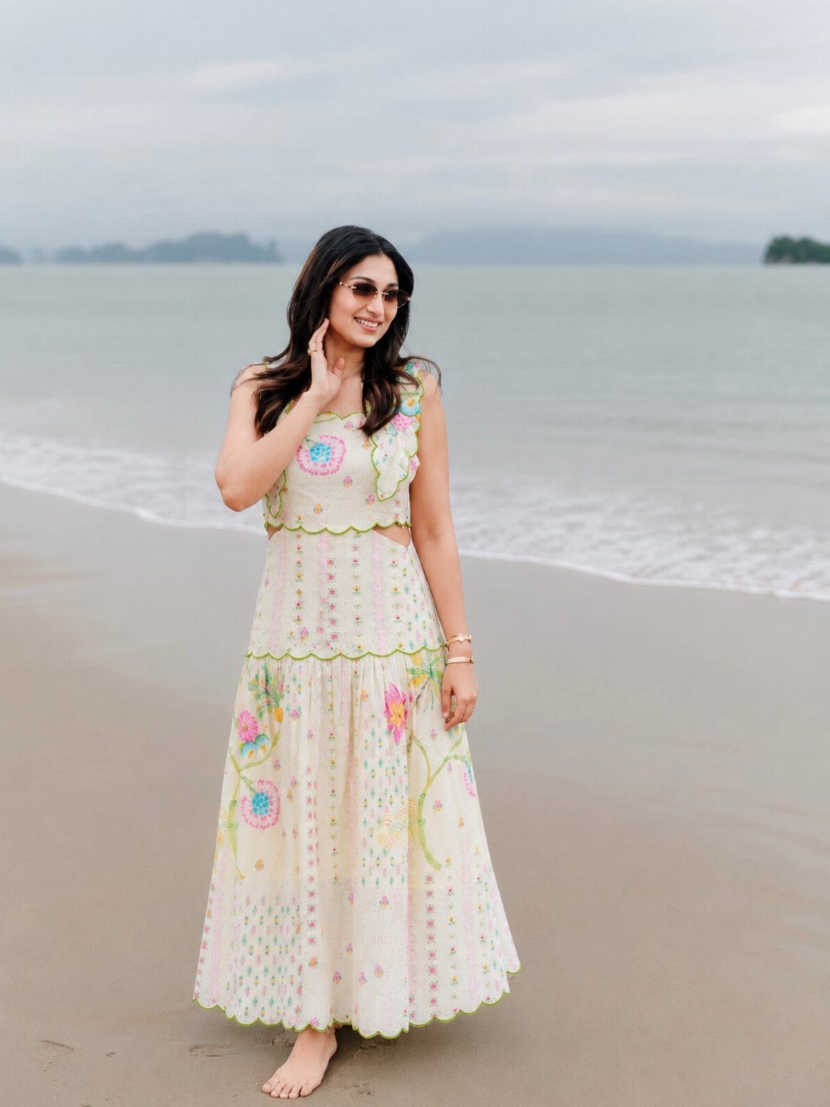 Woman in a white floral embroidered maxi dress standing on a sandy beach.