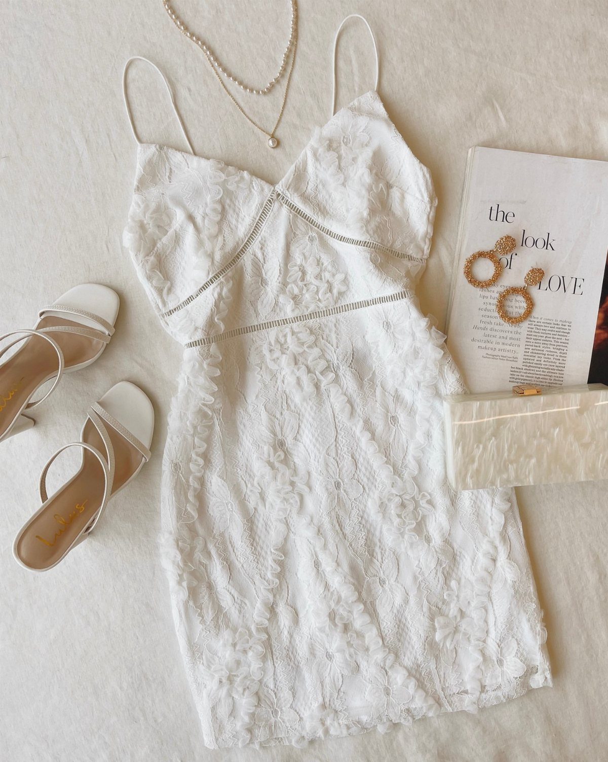 White lace mini dress with matching sandals, pearl necklace, and white clutch bag.
