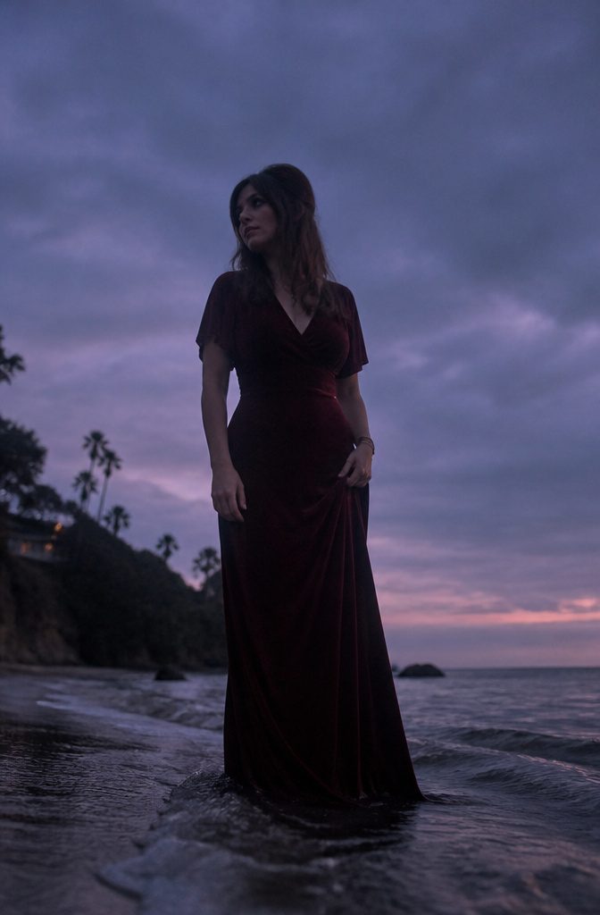 Lana Del Rey by the water at dusk with a moody atmosphere.