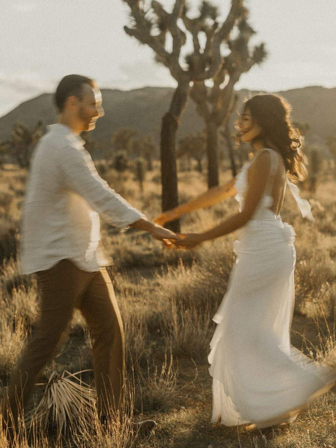 Couple holding hands in a desert landscape with Joshua trees at sunset.