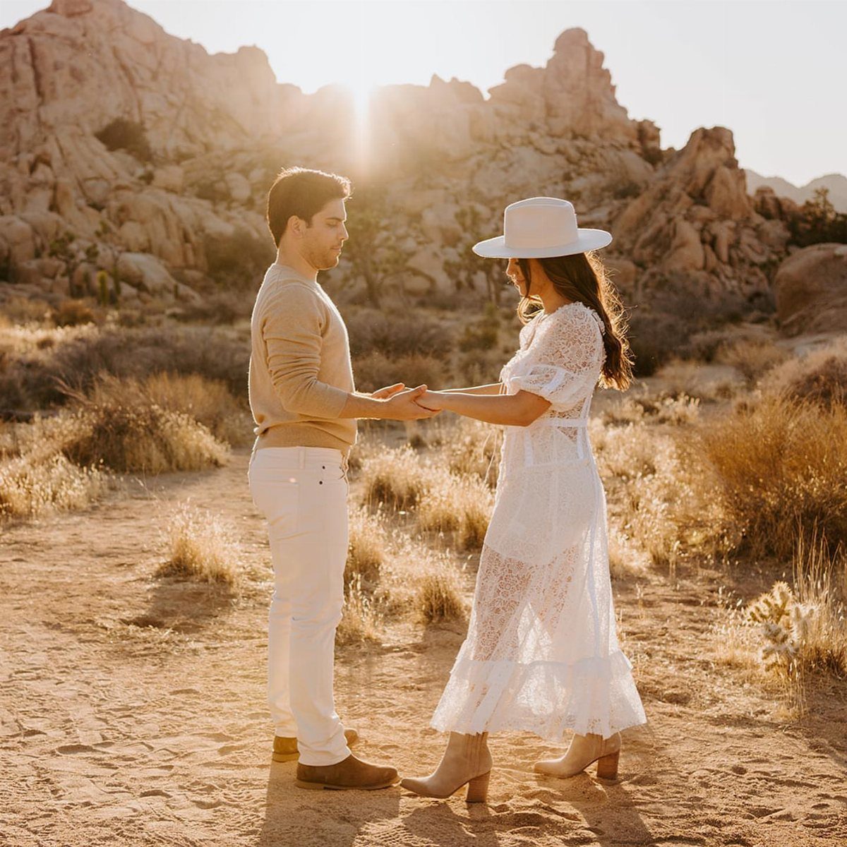 Couple holding hands in a desert landscape with rocky mountains and bright sunlight.