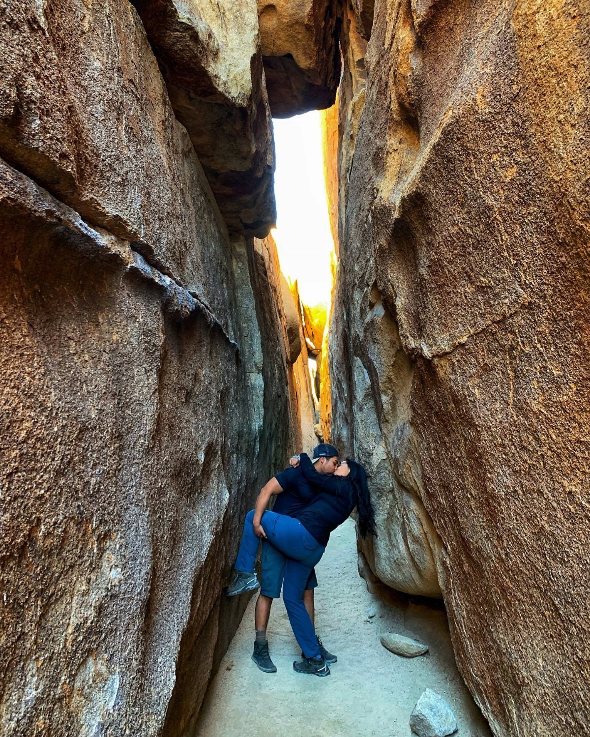 Couple kissing in a narrow desert canyon between towering brown rock walls.