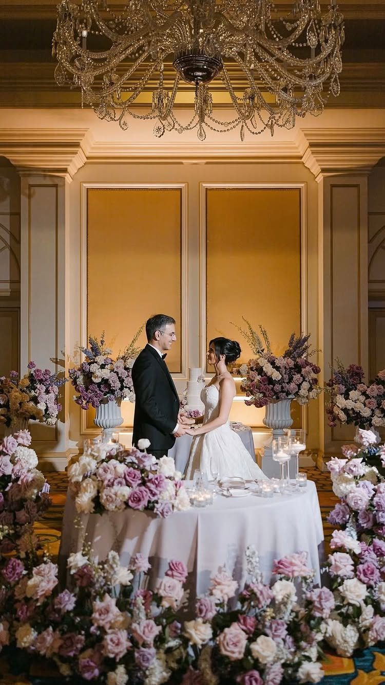 Bride and groom facing each other in a luxury ballroom with lavish floral arrangements.