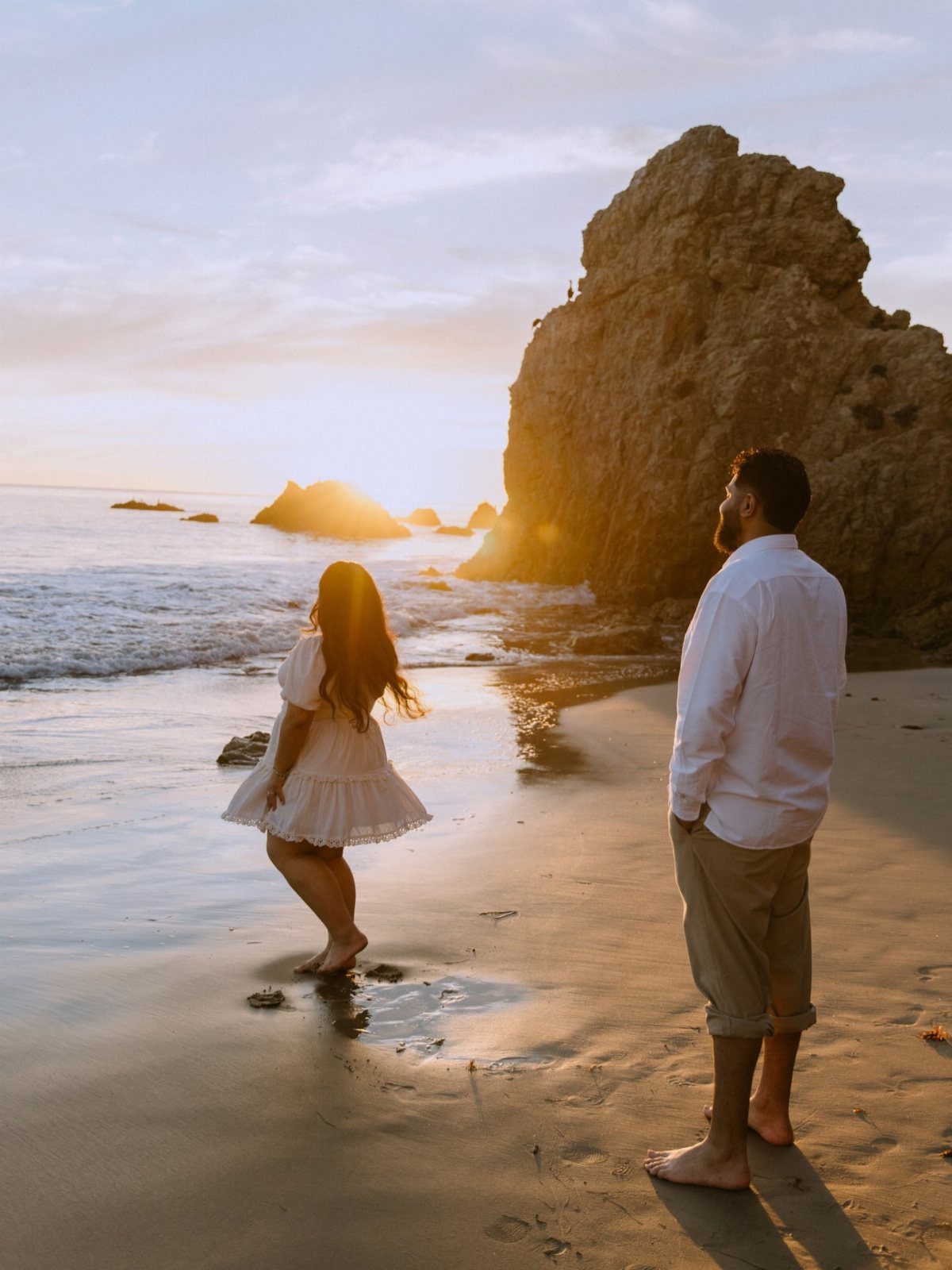 Couple on a beach at sunset with the woman walking toward the water.