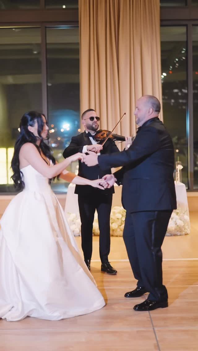 Bride and groom dancing on a wooden floor with a violinist playing behind them.