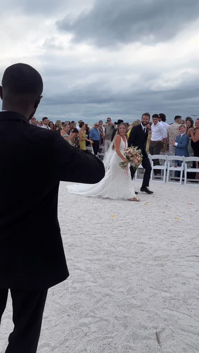 Bride and groom walking down a sandy beach aisle after their wedding ceremony