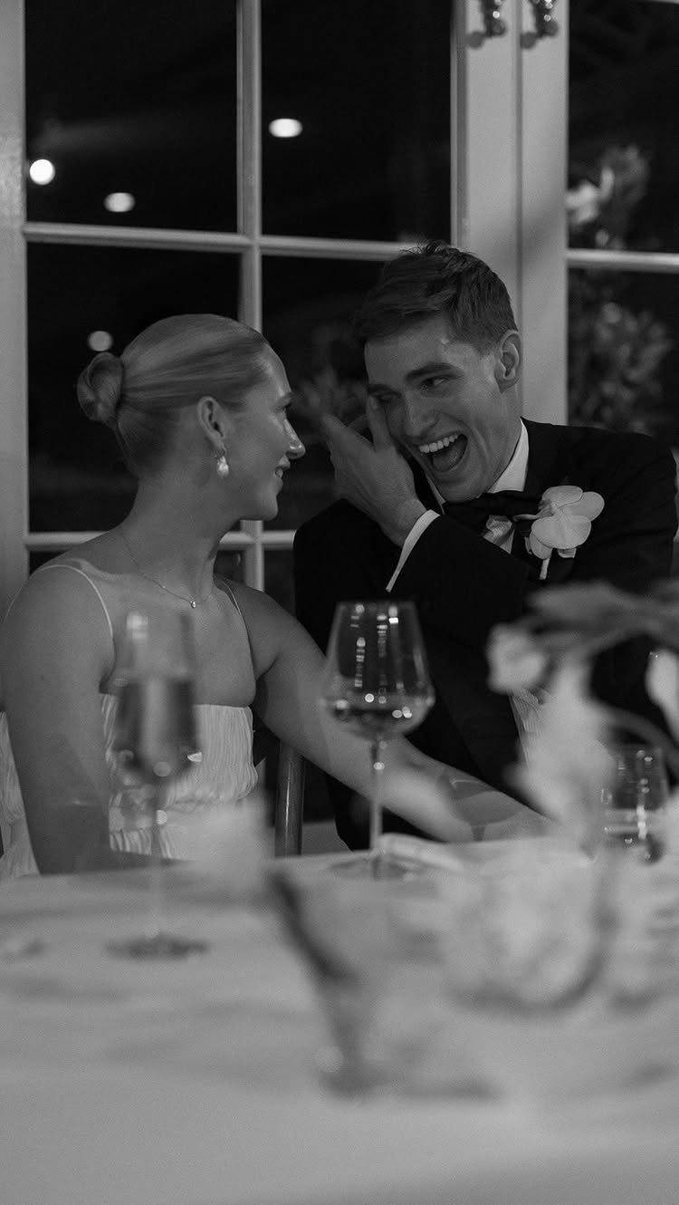 Bride and groom laughing together at a wedding reception dinner table.