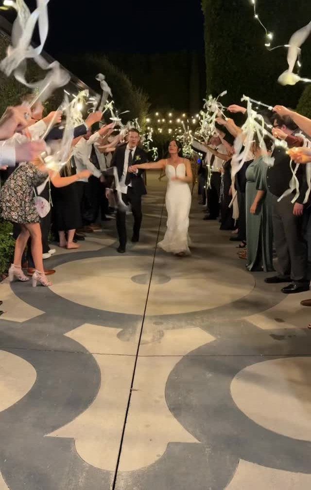 Bride and groom walking through a tunnel of guests waving white ribbons at night
