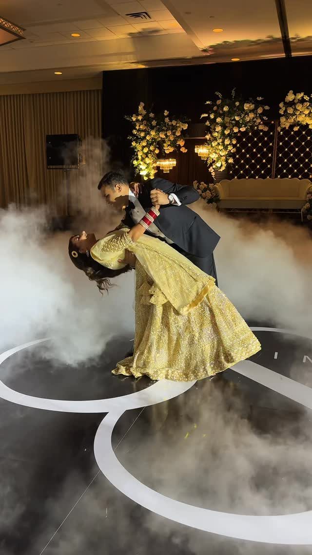 Couple dancing in a ballroom with fog, man dipping woman in gold dress.