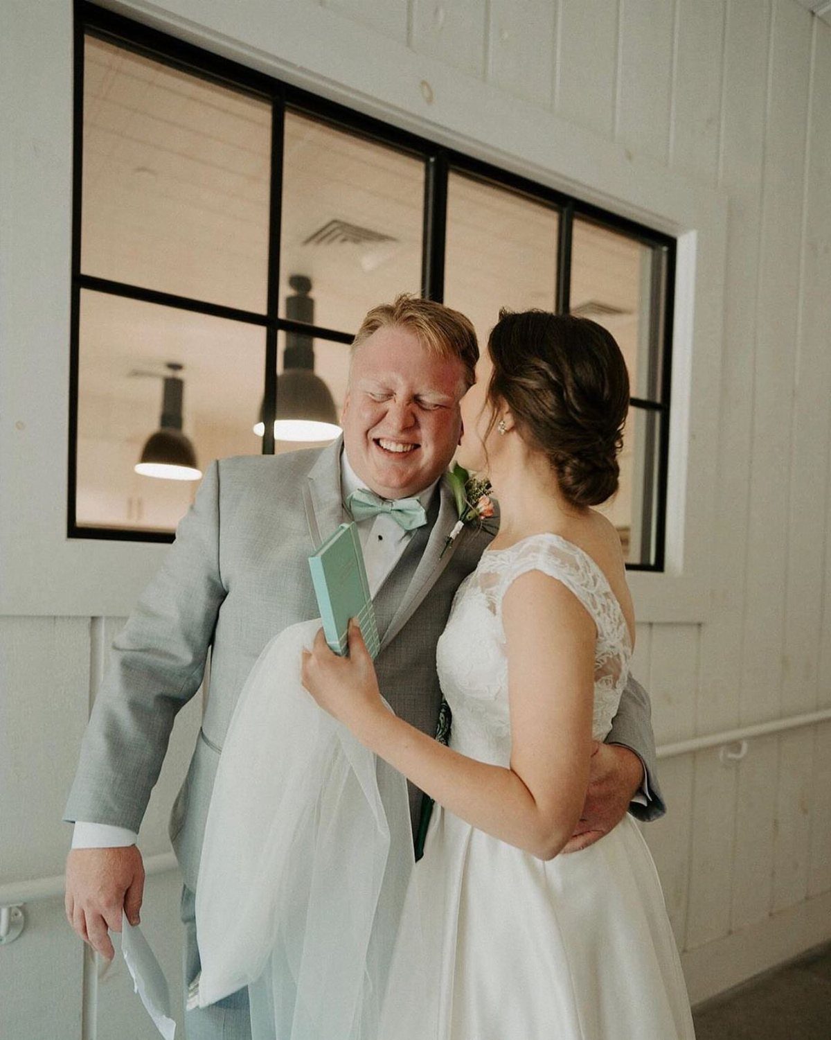 Emotional groom in grey suit embracing bride in white dress during first look.