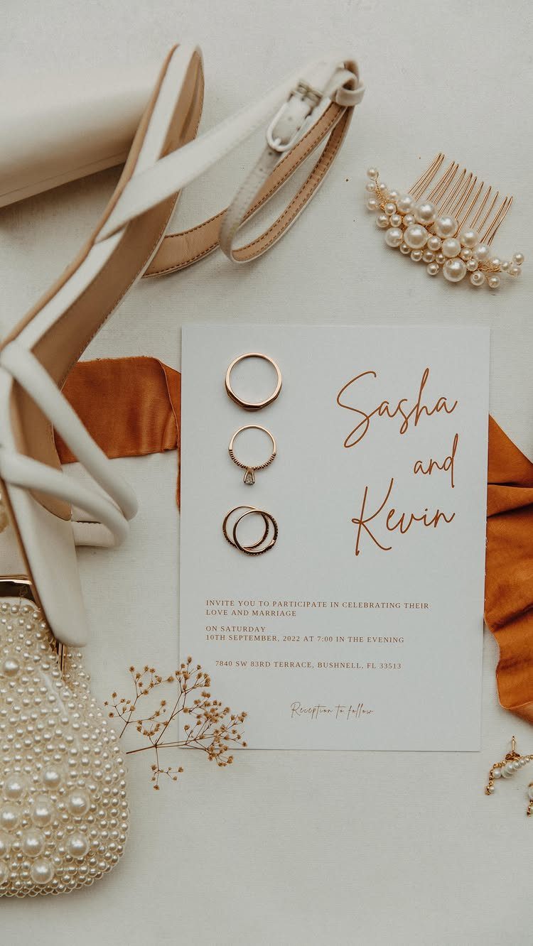 Wedding invitation card surrounded by gold rings, white heels, and pearl accessories.