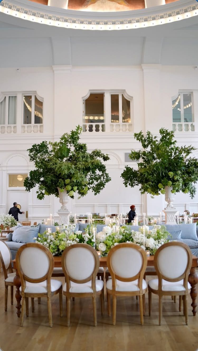 Elegant wedding reception table with white chairs and large green floral arrangements.