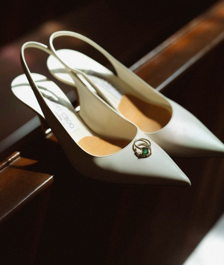 White slingback wedding shoes with gold rings resting inside on dark wood.