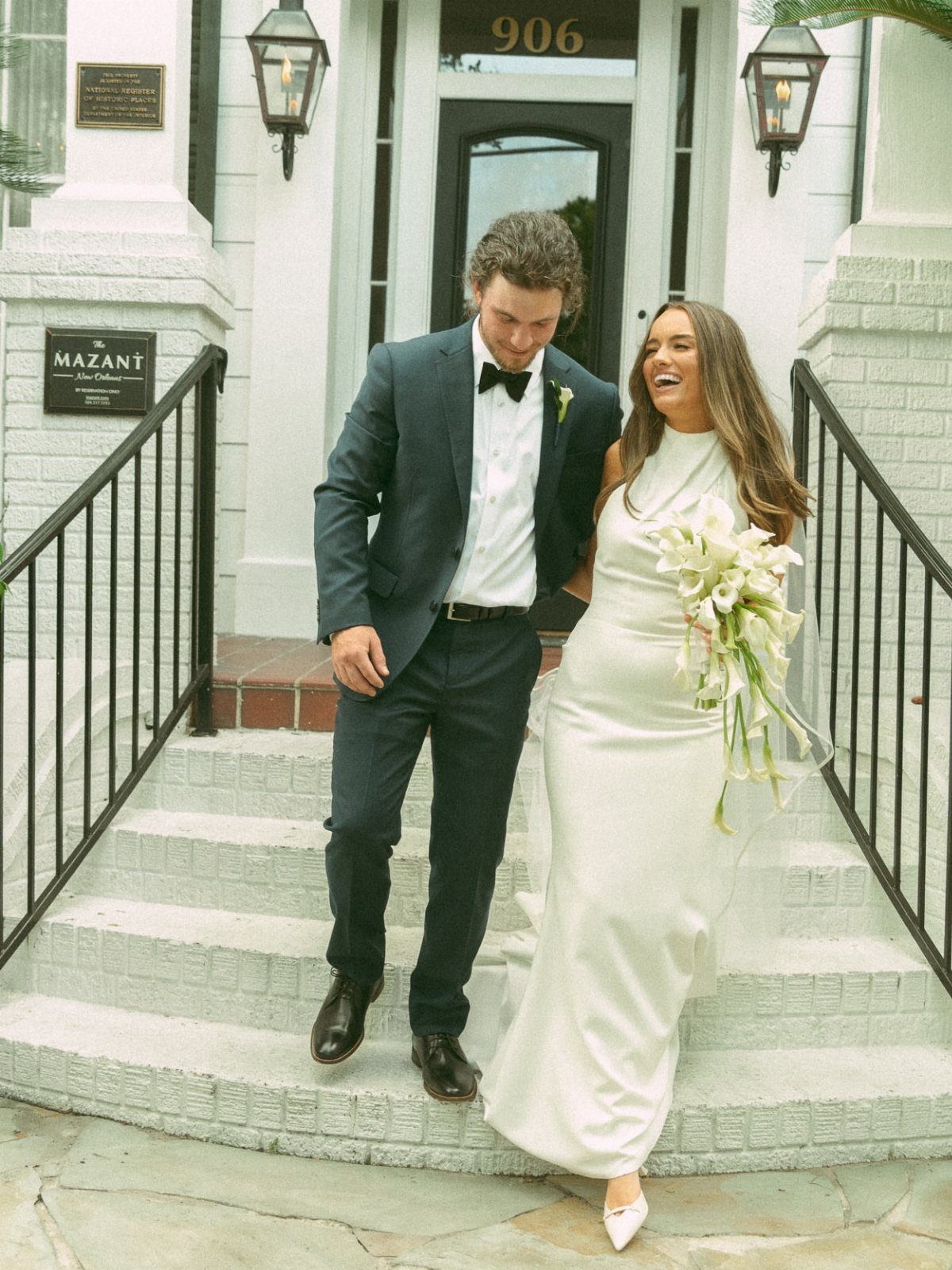 Bride and groom laughing while walking down white steps outside a historic building.