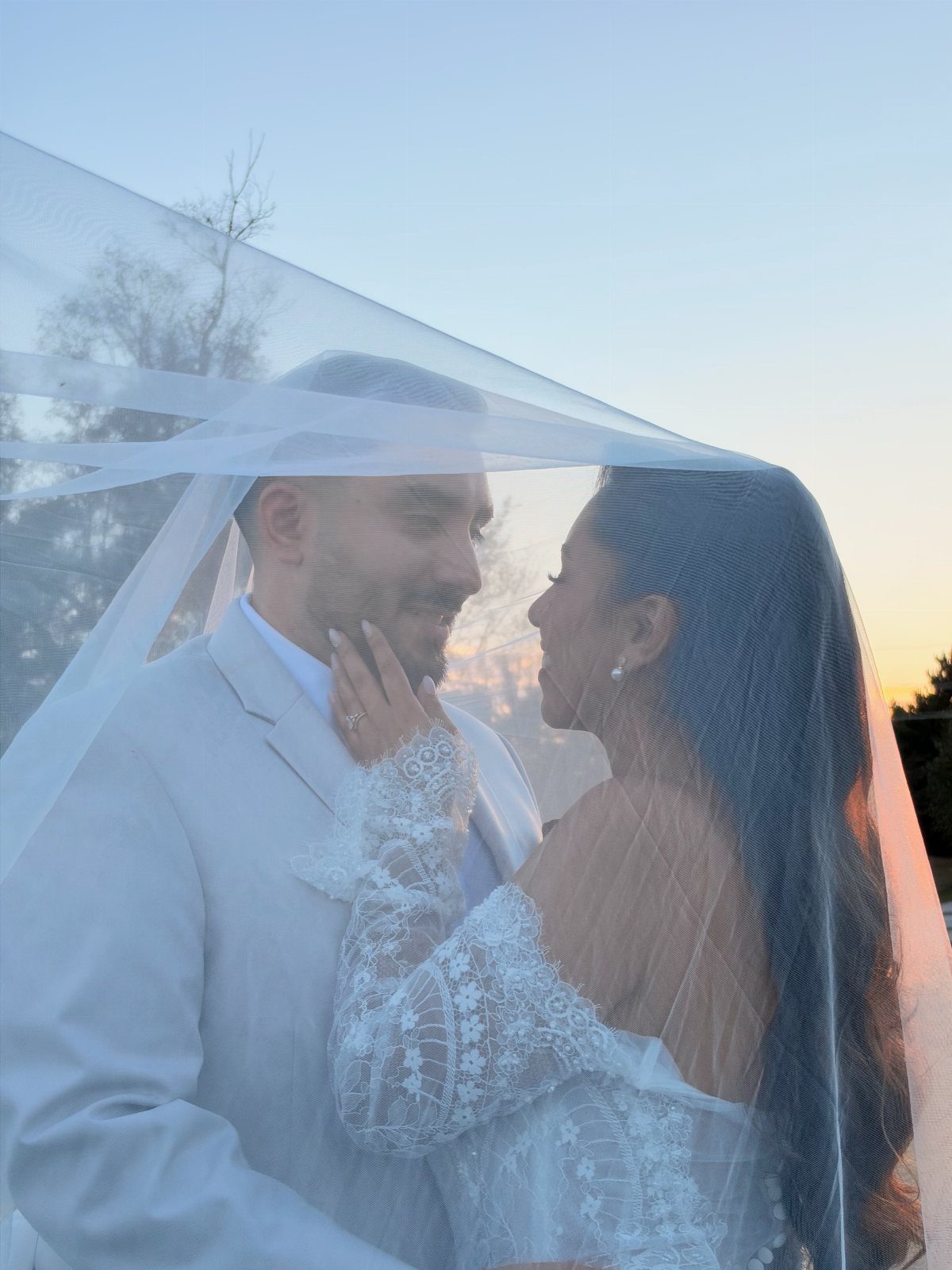 Bride and groom gazing at each other under a sheer white wedding veil.