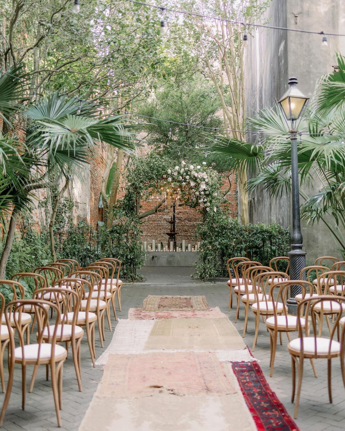 Outdoor wedding ceremony setup with vintage rugs and floral arch in a historic courtyard.