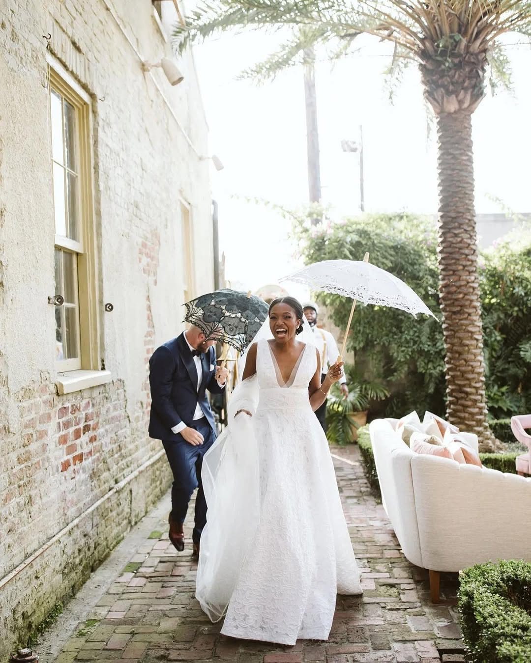 Bride and groom walking on a brick path with lace parasols in New Orleans