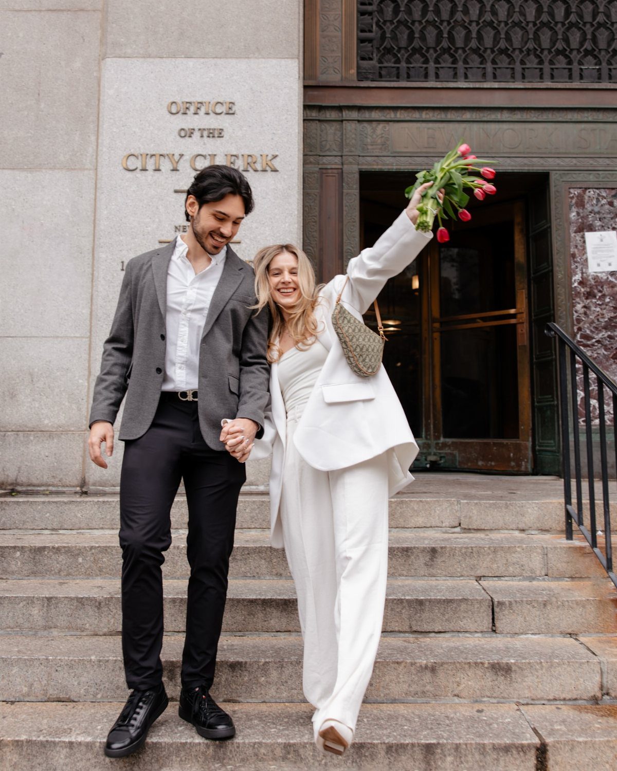 Newlywed couple walking down stone steps outside the Office of the City Clerk.