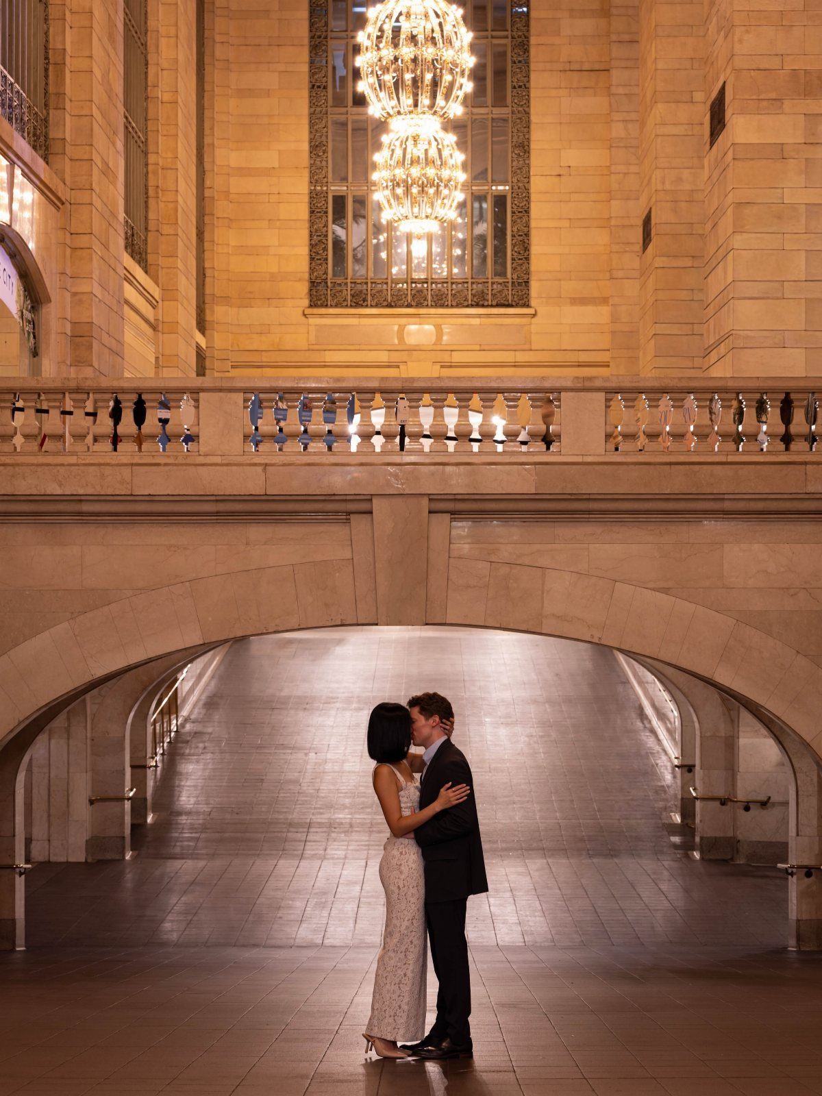 Couple in wedding attire kissing under a marble archway in a grand hall.
