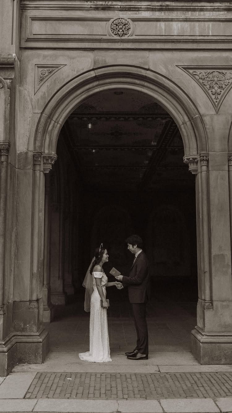 Bride and groom standing under a stone archway during a low-key wedding ceremony.