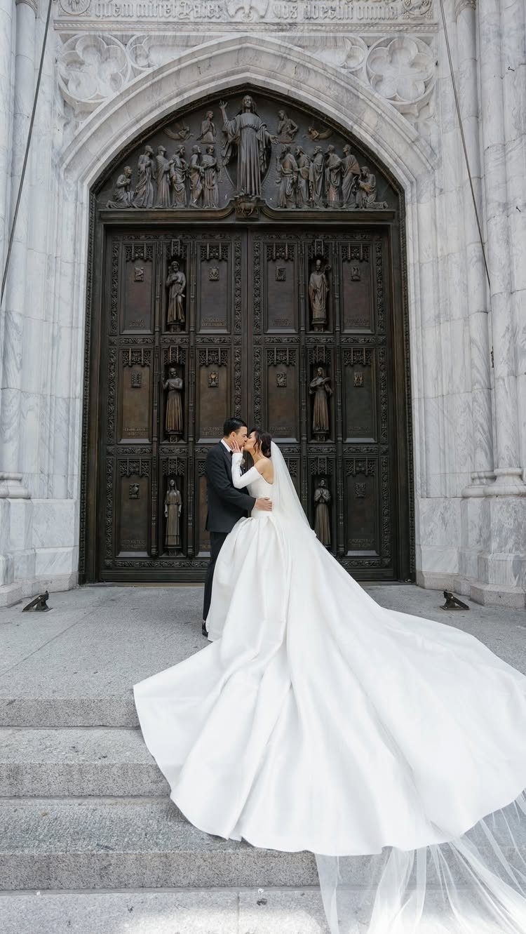 Bride and groom kissing in front of ornate bronze doors of a stone building.