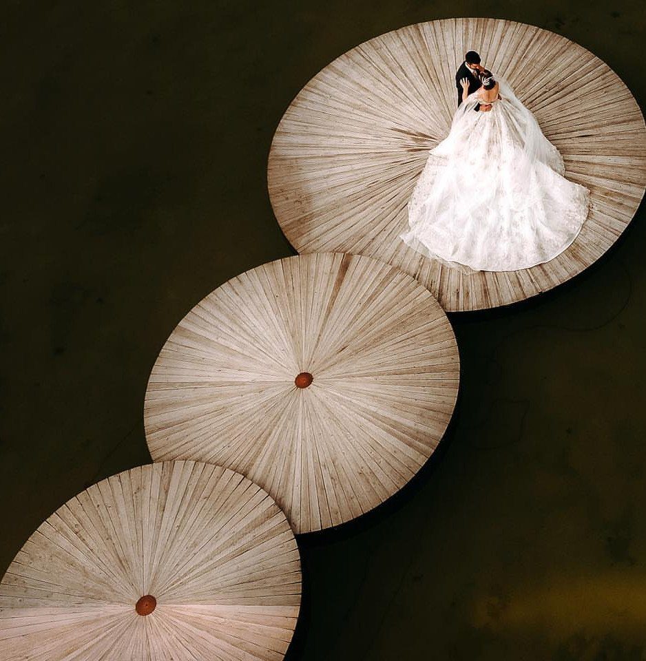 Bride and groom embracing on a circular wooden platform viewed from directly above.