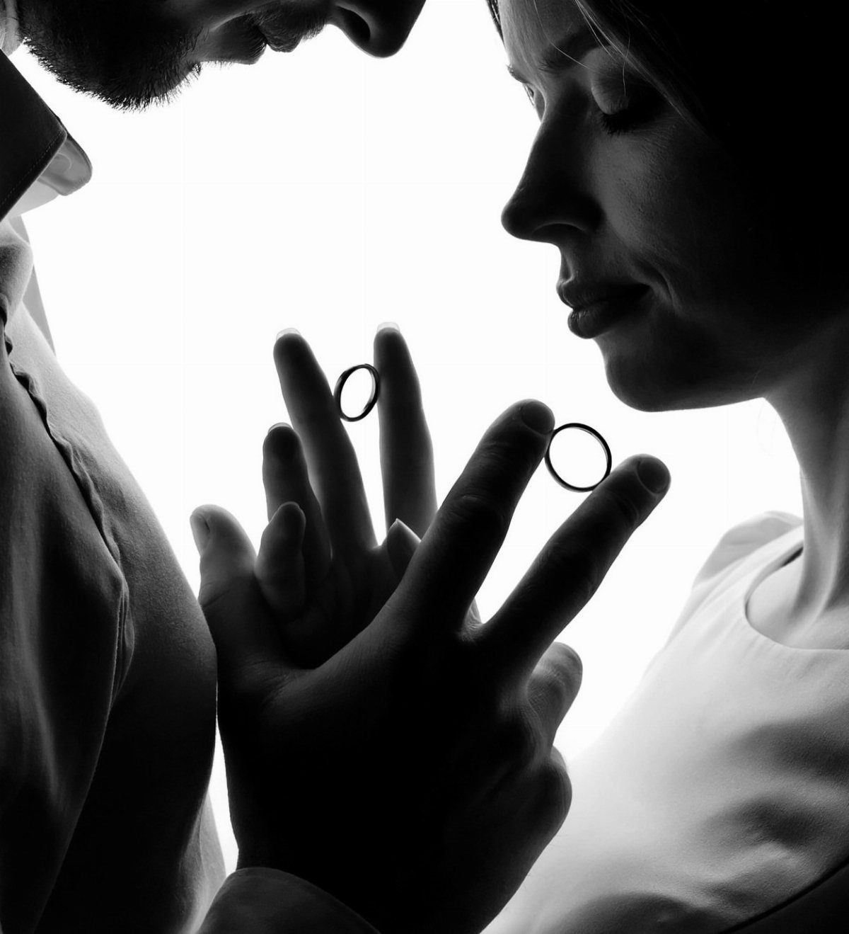 Silhouette of a couple with wedding rings balanced on their fingertips in black and white.