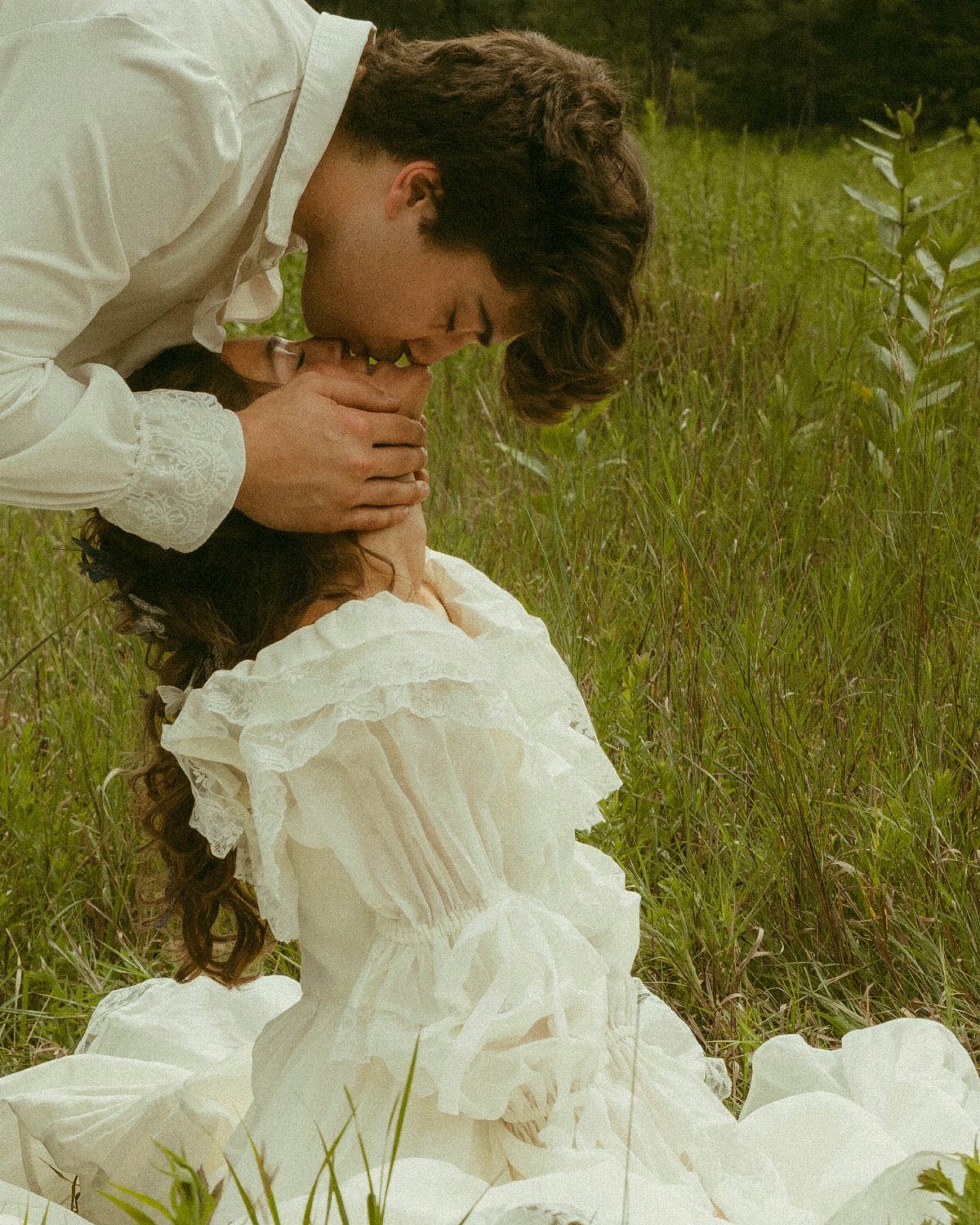 Couple in white attire embracing and kissing in a lush green grassy field.