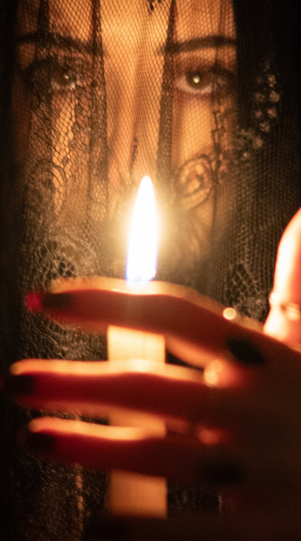 Person behind a black lace veil holding a lit candle in dark lighting