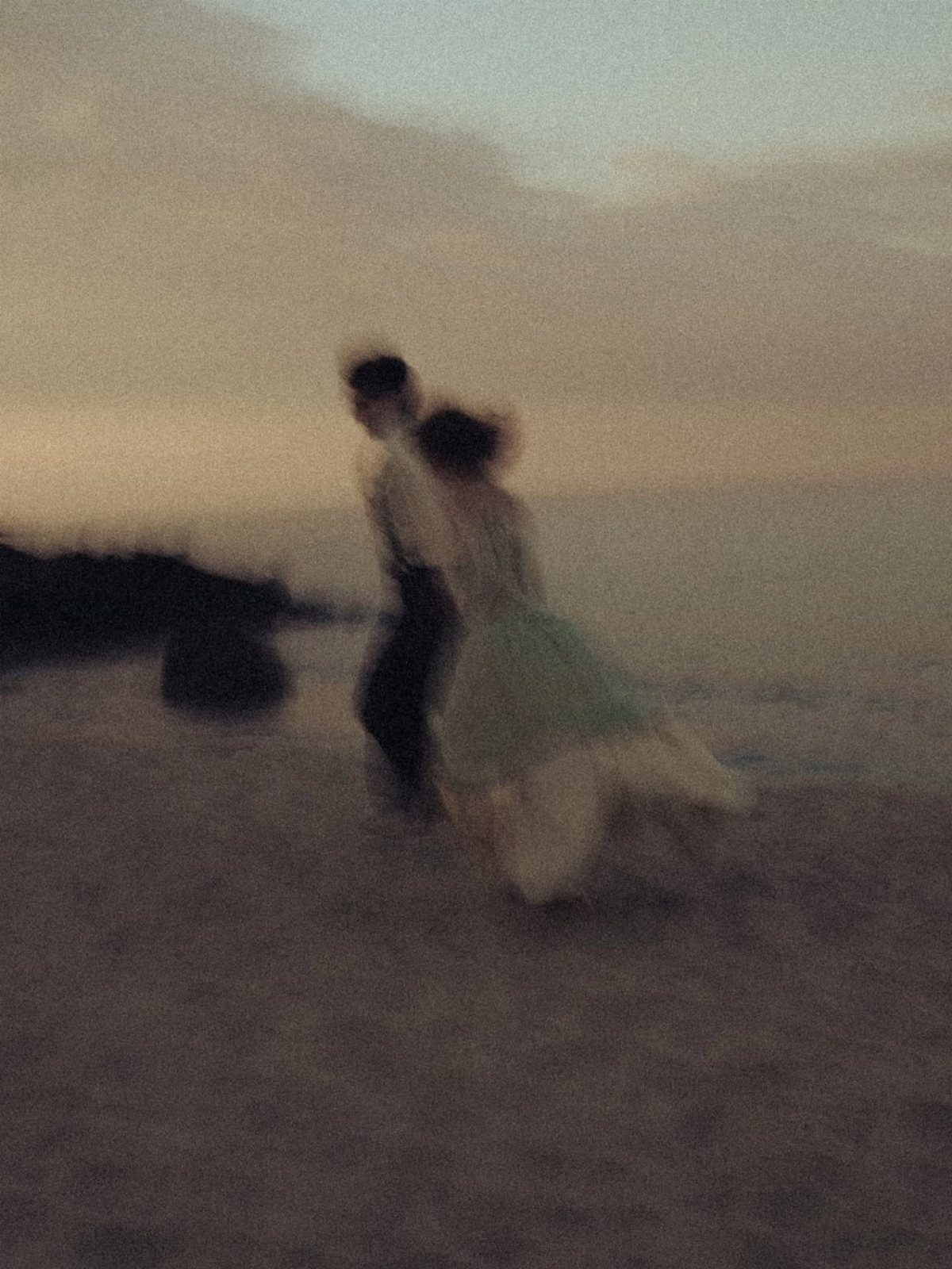 Blurry couple dancing on a beach at dusk with a grainy film effect