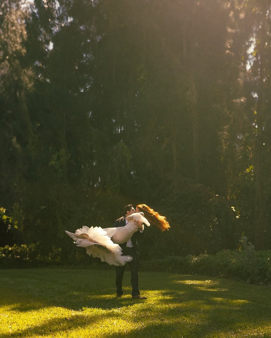 Couple kissing in a field, man lifting woman in a white dress.