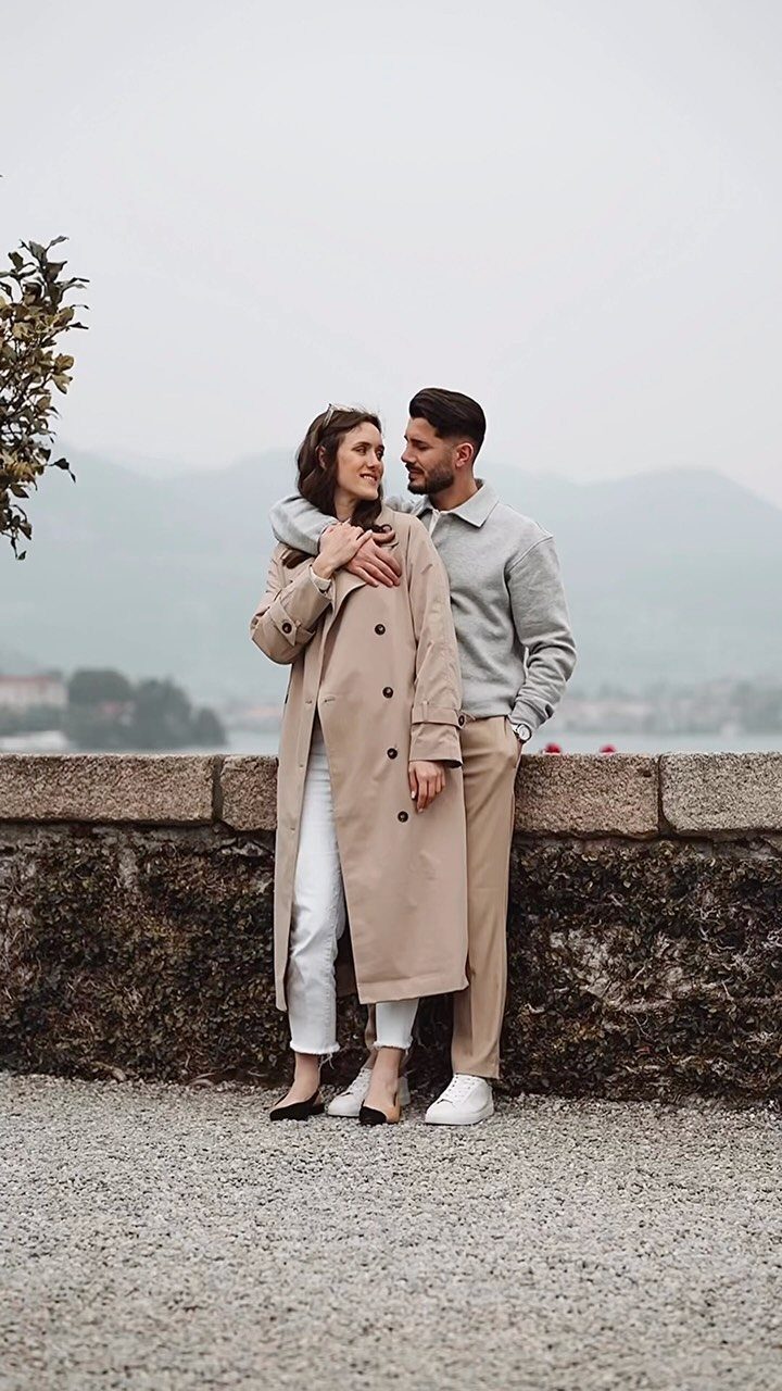 Couple embracing by a stone wall with a hazy mountain landscape behind them.