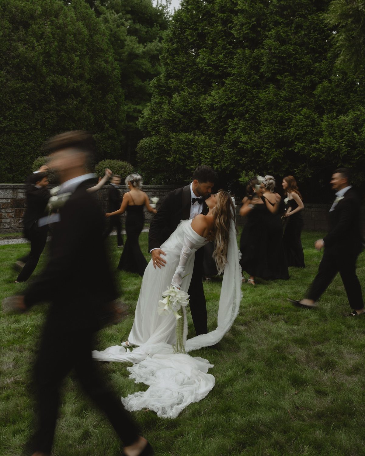 Bride and groom kissing in a grassy field surrounded by wedding guests.