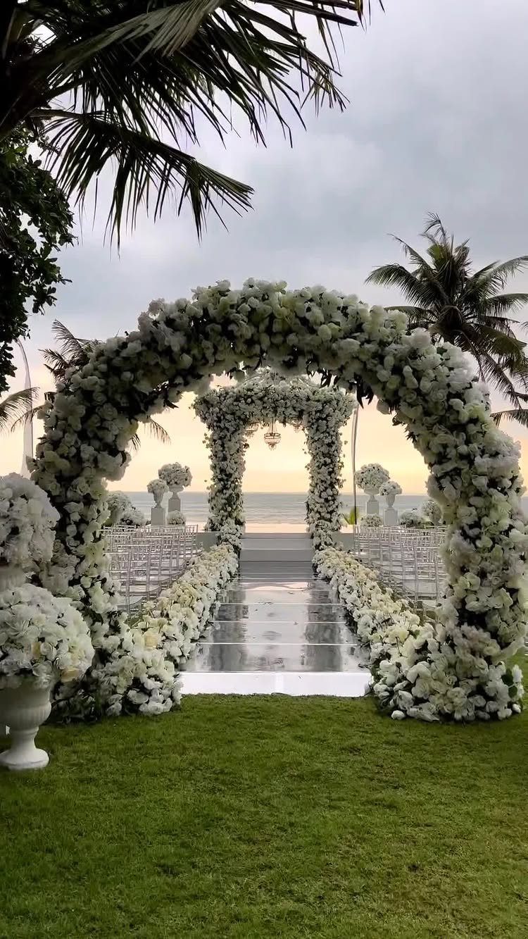 White floral wedding arches and aisle on a lawn overlooking the ocean.
