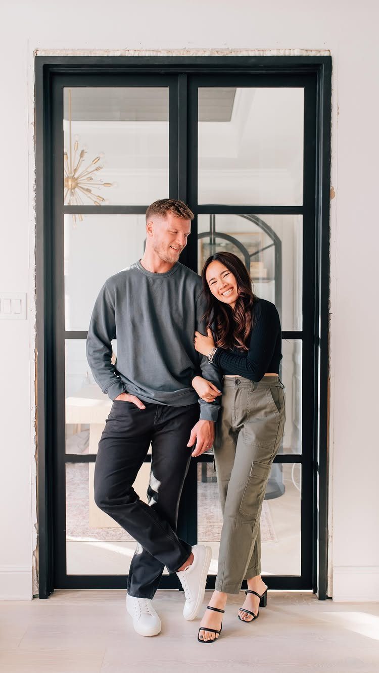 Smiling couple posing in casual grey, black, and olive green outfits by a door